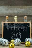 Welcome 2018 written on slate board with baubles and champagne bottle