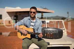 Man playing guitar while sitting on a car