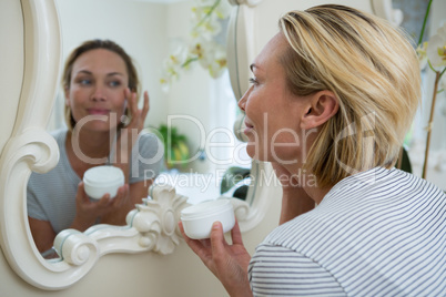 Woman applying moisturizer in bathroom