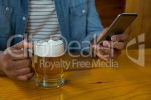 Mid section of man with glass of beer using mobilephone