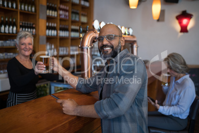 Senior waitress serving glass of beer to customer at counter