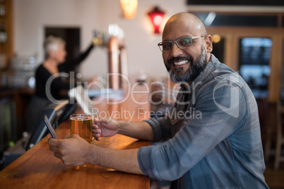 Smiling man using mobile phone while having beer at counter in restaurant
