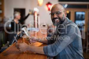 Smiling man using mobile phone while having beer at counter in restaurant