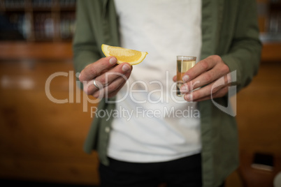 Man holding tequila shot and lemon wedge in bar