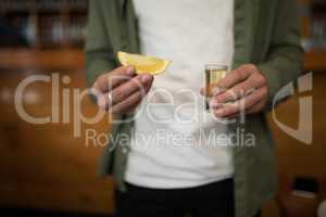 Man holding tequila shot and lemon wedge in bar