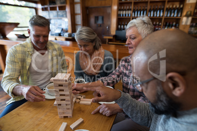 Happy friends playing jenga game while having cup of coffee