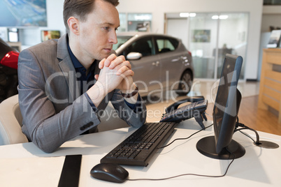 Salesman using computer while working in car showroom