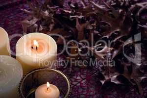 Lit candles and dry leaves on table