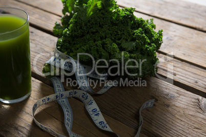 Mustard greens, measuring tape and juice on wooden table