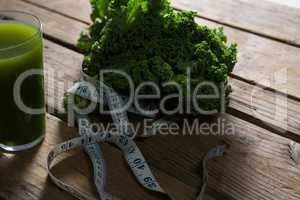 Mustard greens, measuring tape and juice on wooden table