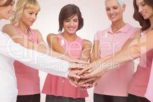 Composite image of female friends stacking hands for breast cancer awareness