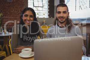 Portrait of young friends with laptop at cafe