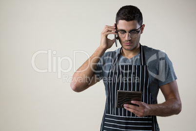 Waiter looking at the digital tablet while talking on the mobile phone