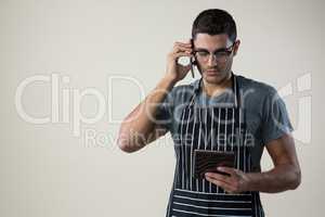 Waiter looking at the digital tablet while talking on the mobile phone