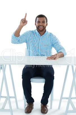 Male executive pointing upwards while sitting at desk