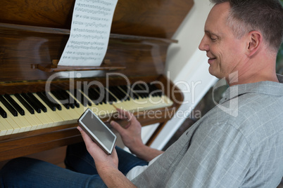 Man using digital tablet while playing piano