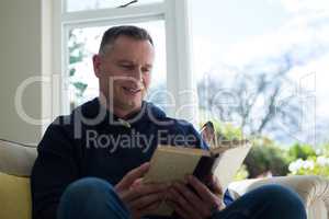 Man reading novel on sofa in living room