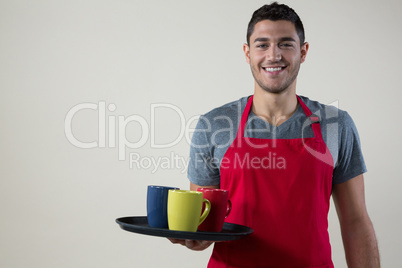 Smiling waiter holding a tray with coffee cups