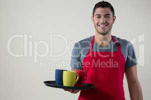 Smiling waiter holding a tray with coffee cups