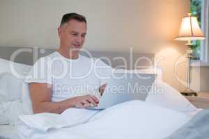 Man using laptop on bed in bedroom