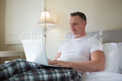 Man using laptop on bed in bedroom