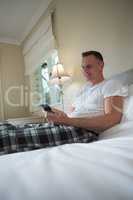 Man using mobile phone on bed in bedroom
