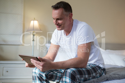 Man using digital tablet on bed in bedroom