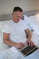 Man using laptop on bed in bedroom