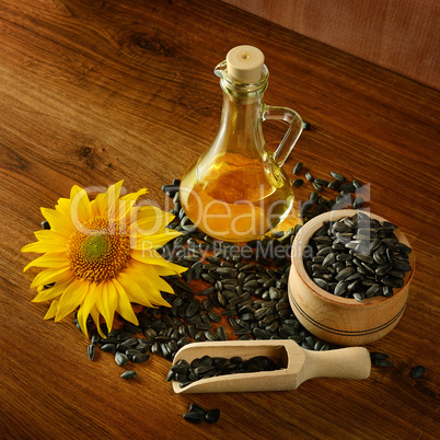 Seeds, oil and sunflower flower on wooden background