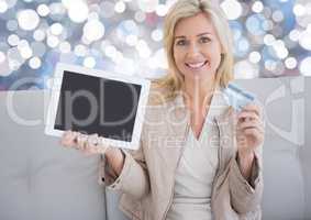 Woman holding tablet with bank card and sparkling lights background