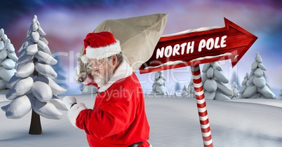 North Pole text and Santa holding sack with Wooden signpost in Christmas Winter landscape
