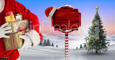 Santa holding gifts and Wooden signpost in Christmas Winter landscape with Christmas tree