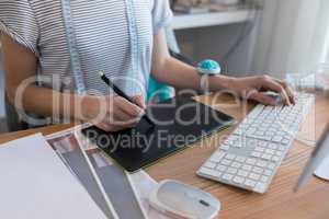 Mid section of female designer using graphic tablet at desk