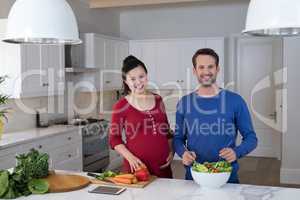 Pregnant couple preparing salad in the kitchen