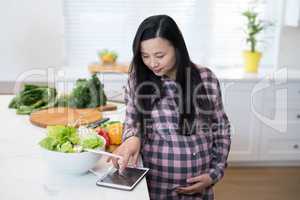 Pregnant woman using digital tablet in kitchen