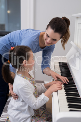 Mother assisting daughter in playing piano