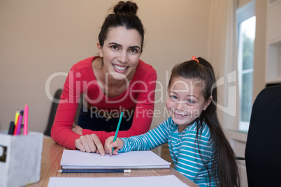 Mother assisting daughter while writing in paper