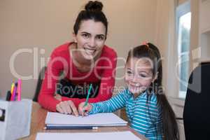 Mother assisting daughter while writing in paper