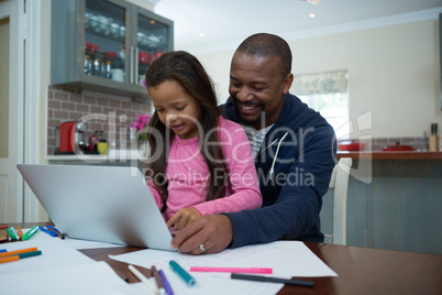 Father and daughter using laptop in kitchen