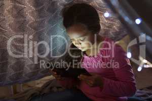 Girl using digital tablet under blanket in bedroom