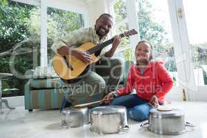 Father and daughter playing with guitar and utensils in living room