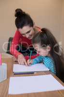 Mother assisting daughter while writing in paper