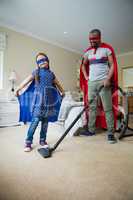 Daughter posing while father cleaning a floor with vacuum cleaner
