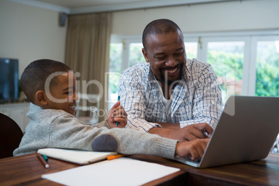 Father and son using laptop in living room