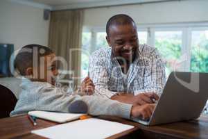 Father and son using laptop in living room