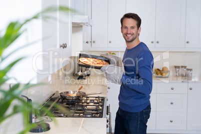 Smiling man holding baked pizza in kitchen