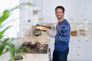 Smiling man holding baked pizza in kitchen