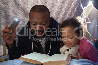 Father and daughter reading book in bedroom