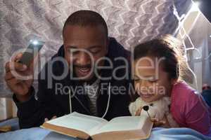 Father and daughter reading book in bedroom