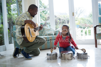 Father and daughter playing with guitar and utensils in living room